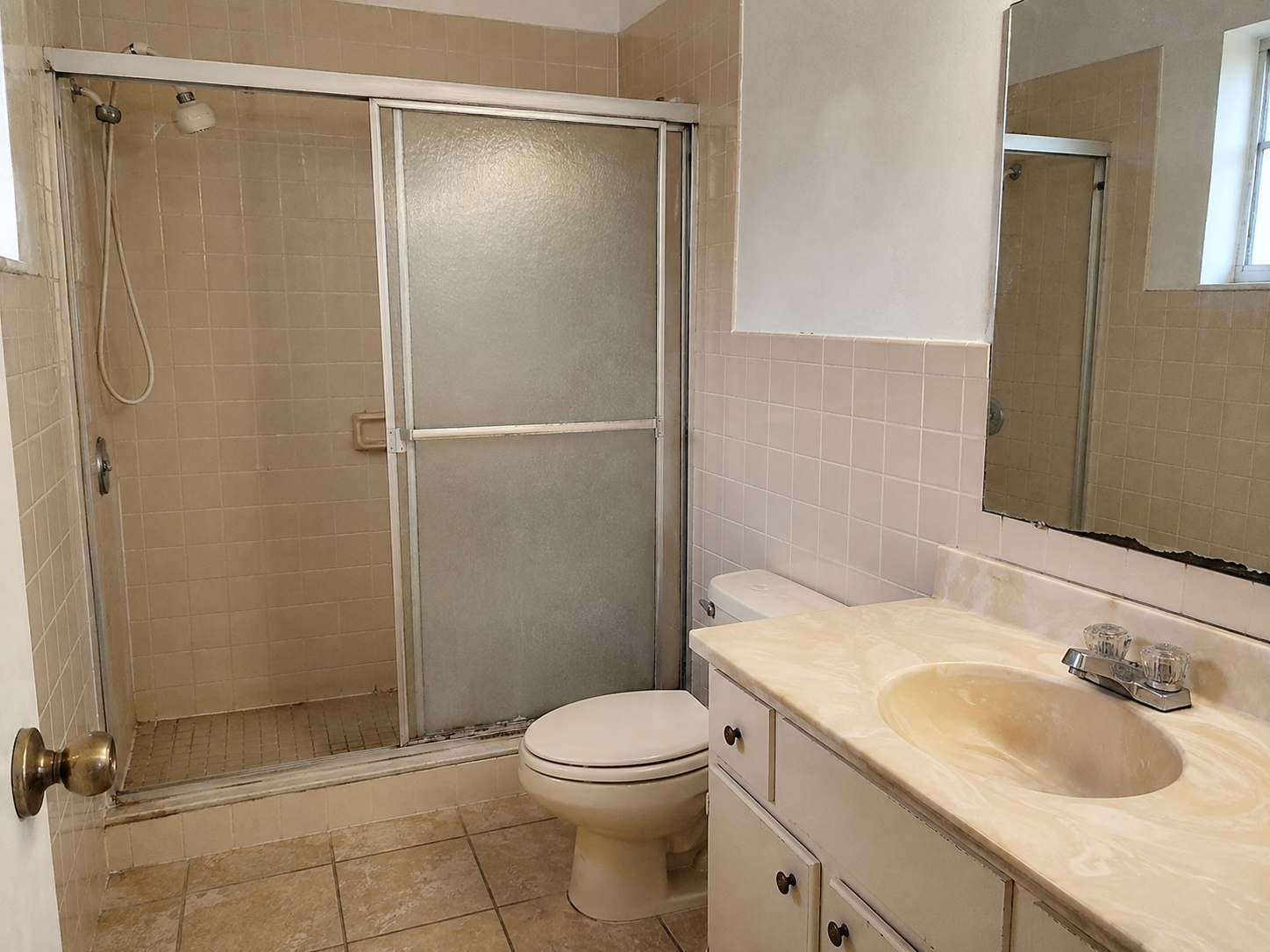 Illustrative image of dated tile, vanity, and shower glass before remodeling
